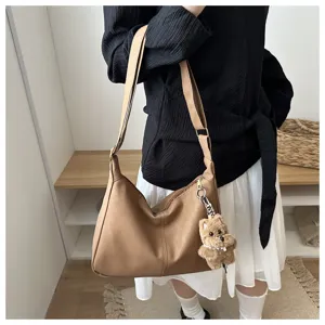 Sac hobo minimaliste en cuir marron avec un porte-clé ours en peluche sur un modèle.