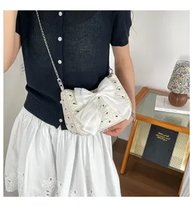 Detail view of a white seersucker shoulder bag with a large bow and chain strap.