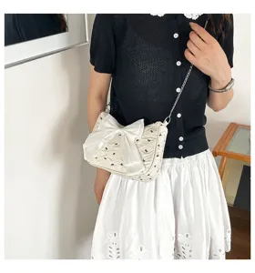 Detail view of a stylish white bubble gauze crossbody bag with a large bow worn by a model.