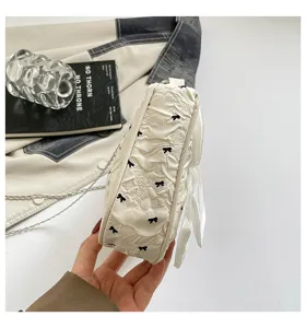 Side view detail of a stylish white bubble gauze shoulder bag with black bow accents