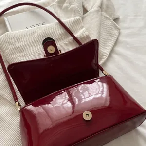Close-up of dark red patent leather bag showing metal magnetic buckle closure