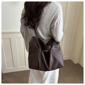 Large brown minimalist tote bag shown worn on shoulder by model for daily commuting style.