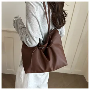 Close-up detail of a large brown pebbled leather tote bag worn as a casual shoulder bag