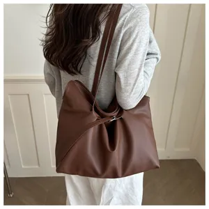 Large brown leather tote bag worn by a model in a minimalist indoor commuter setting.