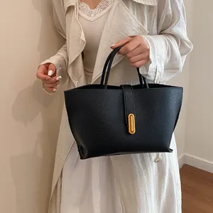 Elegante bolso tote de cuero negro con herrajes dorados sostenido por una modelo
