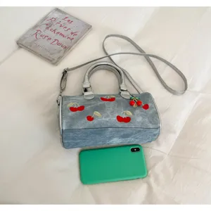 Detailed top view of cherry embroidered denim Boston bag with phone for scale reference
