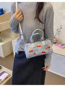 Detail view of denim Boston bag with embroidered cherries and silver straps on model
