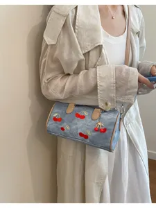 Detail of cherry embroidered denim Boston bag worn with a beige trench coat