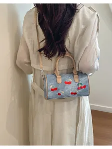 Back view of a cherry embroidered denim Boston bag worn with a stylish beige trench dress