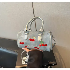 Close-up of denim Boston bag featuring red cherry embroidery and silver hardware details