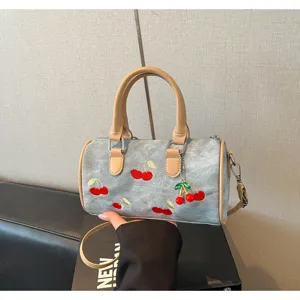 Detail view of denim Boston bag featuring red cherry embroidery and tan leather handles.