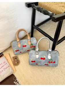 Embroidered cherry denim Boston bags with tan and silver handles on a beige rug