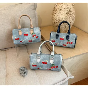 Detailed view of three embroidered cherry denim Boston bags in various handle colors