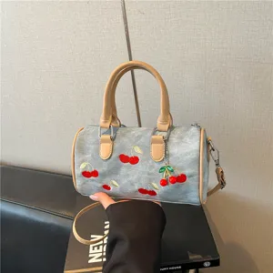 Stylish cherry embroidered denim Boston bag featuring tan handles and a detachable strap.