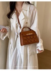 Detail showing a minimalist brown leather crossbody square bag styled with a white trench coat