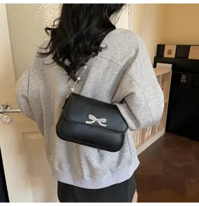 Elegante schwarze Achseltasche mit Kristallschleife, getragen von einem Model im Innenraum.