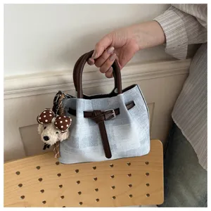 Macro view of blue fabric handbag featuring brown leather straps and a plush charm