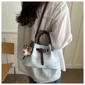 Detail of retro blue denim bucket bag with plush bear charm shown on model shoulder