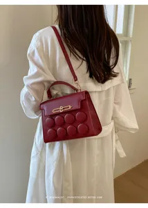Detail view of a red minimalist small square handbag worn over a white trench coat