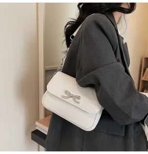 Detailansicht einer weißen Unterarmtasche mit eleganter Strass-Schleifenschnalle.