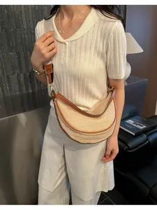 Sac bandoulière en paille en forme de croissant porté par un mannequin élégant.