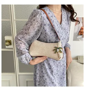 Κομψή πλεκτή ψάθινη τσάντα ώμου με τροπικό φοίνικα φορεμένη από μοντέλο για παραλία