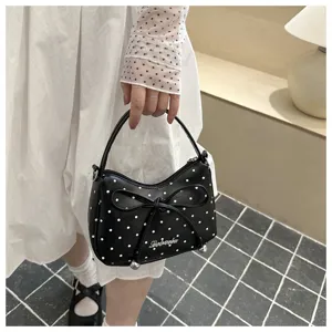 Detailopname van een trendy zwarte handtas met polkadots en een decoratieve strik.