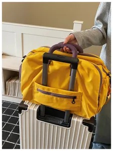 Detailansicht der gelben Reisetasche mit Kofferhaltegurt auf einem Rollkoffer.