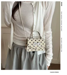 Détail d'un sac à bandoulière beige à pois avec un nœud scintillant sur un mannequin