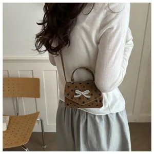 Sac bandoulière marron à pois avec un nœud en strass porté par un mannequin de dos.