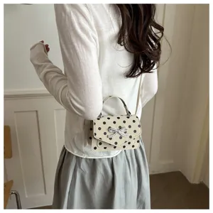 Vue détaillée d'un petit sac à main carré crème à pois noirs avec un nœud en strass