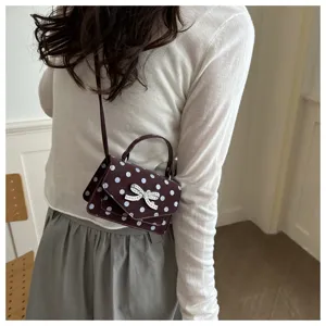Vue détaillée d'un sac à main bordeaux à pois avec nœud en strass sur une femme