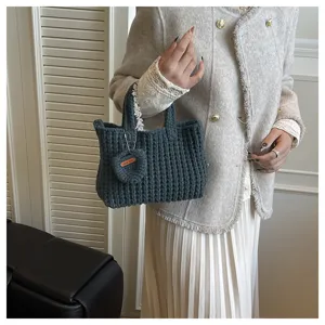 Gros plan d'un sac à main en tricot gris fait main tenu par un mannequin en veste tweed.