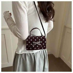 Détail d'un sac à bandoulière bordeaux à pois avec un nœud en strass
