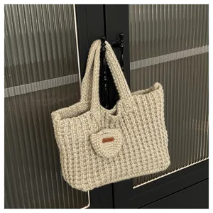 Gros plan d'un sac à main beige tricoté à la main avec un charm en forme de cœur