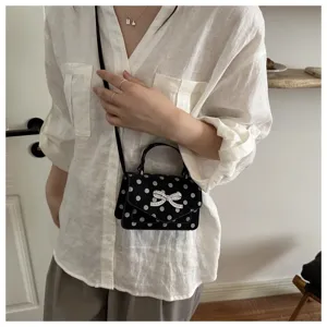 Détail d'un petit sac bandoulière noir à pois avec un nœud en cristal étincelant.