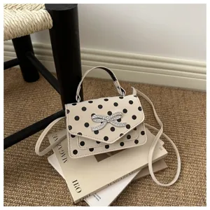 Gros plan d'un sac à main beige élégant à pois avec un nœud en strass étincelant.
