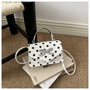Détail d'un sac à main blanc à pois orné d'un nœud décoratif en strass brillant.