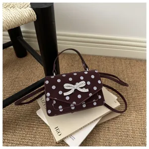 Petit sac à main bordeaux à pois avec nœud en cristal élégant posé sur des livres