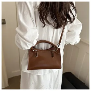 Stylish brown faux leather motorcycle crossbody bag with rivets shown on a model