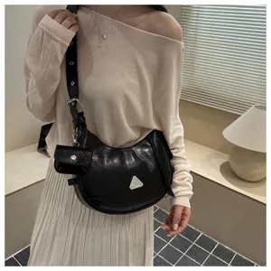 Trendy black hobo moon bag worn on shoulder, featuring a triangle buckle and mini pouch.