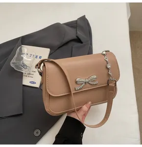 Nahaufnahme einer beigen Achseltasche im süßen Stil mit Strassschleife und Kette.