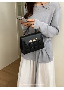Detail of a chic black handbag with unique circular padded design held by a model