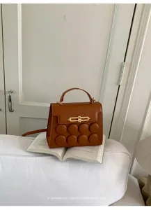 Detail of brown square crossbody bag with padded circular design on white book