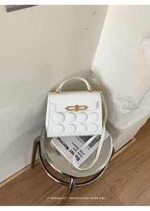 Detailed view of white structured handbag with embossed dots and gold hardware.