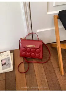 Retro red handbag with unique bubble design and gold clasp detail in home setting