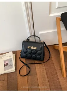 Minimalist black handbag with circular patterns and gold buckle on a wooden floor