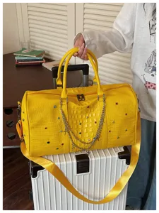 Detailansicht der gelben Reisetasche aus Kroko-Kunstleder mit bunten Strasssteinen und Kreuzketten.