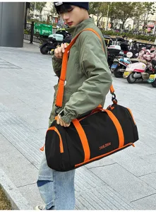 Detail view of the black and orange duffel bag worn by a model in an outdoor street setting.