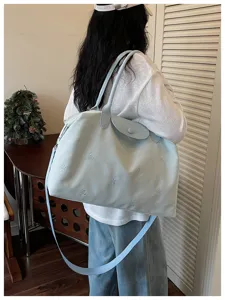 Detailed shot of light blue travel tote bag, large capacity shoulder bag with cute bow embroidery.